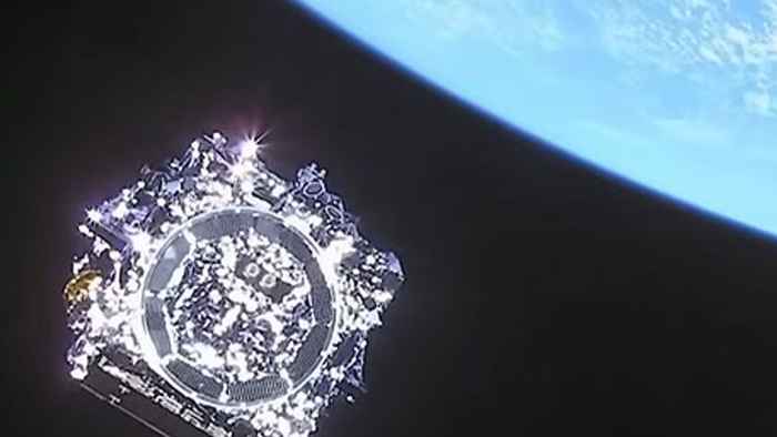 Foto genomen vanuit de ruimte van de James Web Space Telescoop, een glimmend ruimteschip in de vorm van een kubus, met de aarde in de rechterbovenhoek.