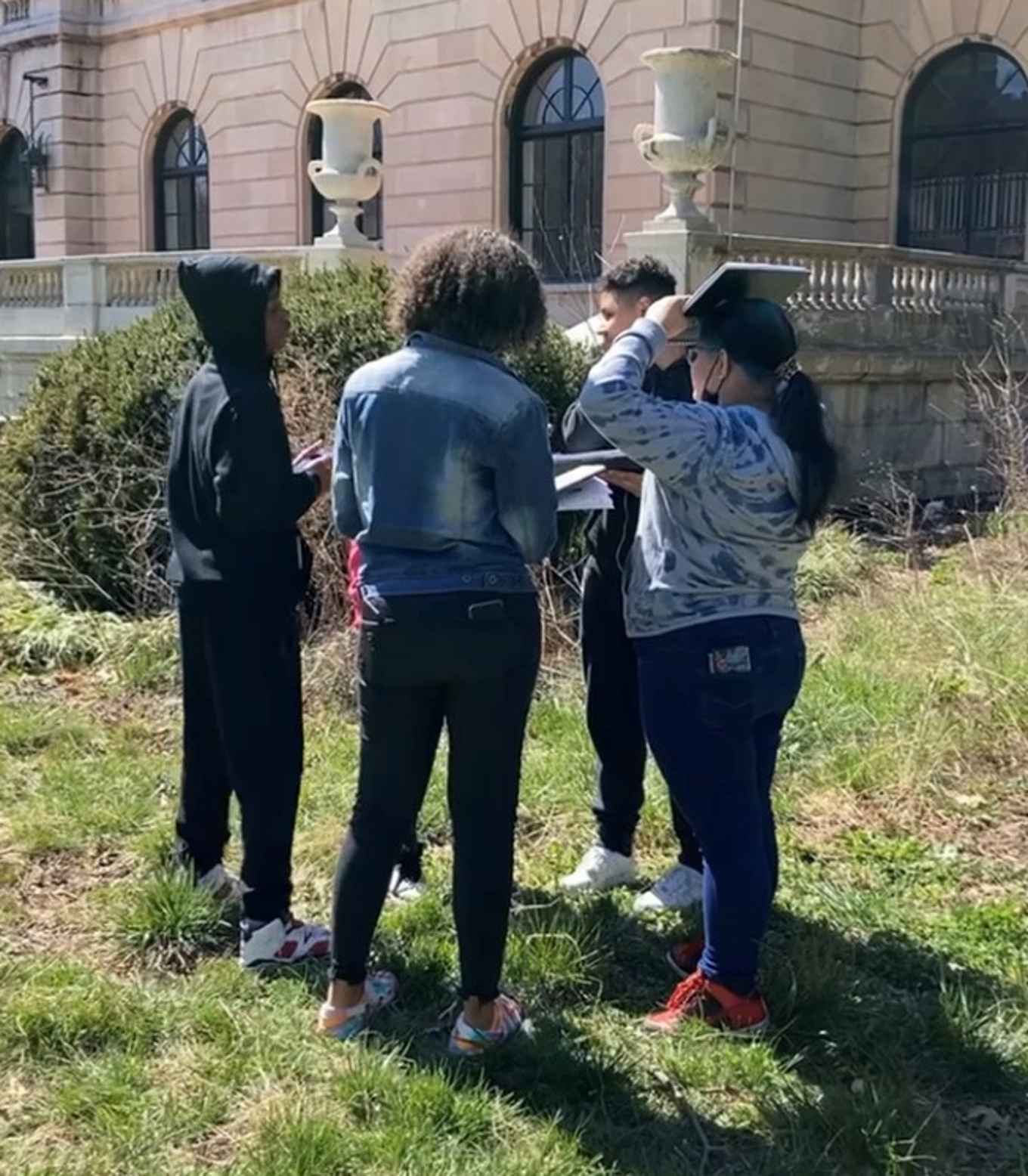 Teens are discussing their plans while standing in a small group outside on the grass