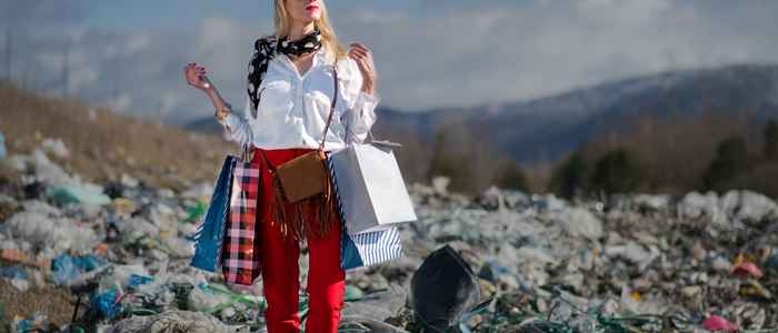 vrouw staat op een grote afvalberg terwijl ze haar 'shopping bags' vasthoudt