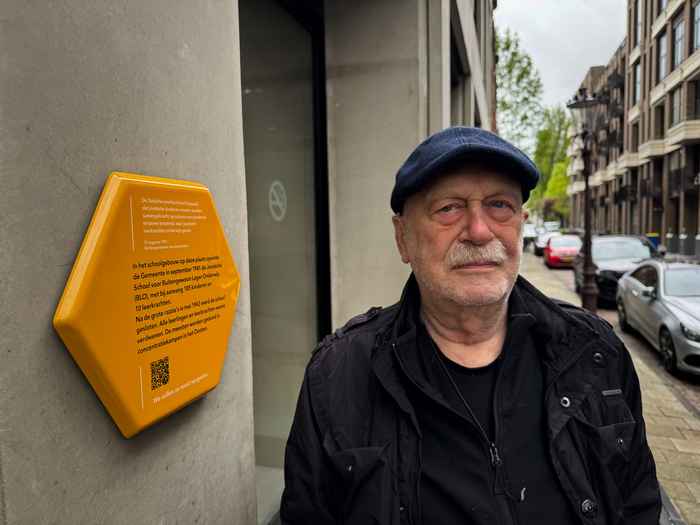 Een man naast een geel zeshoekig herdenkingsplaatje