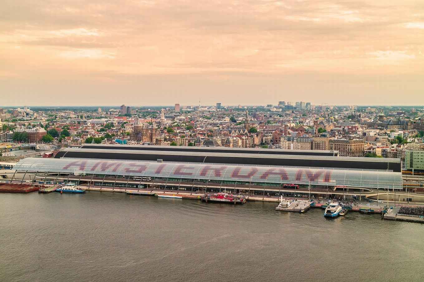 Luchtfoto van Amsterdam bij ondergaande zon met het Ij en Centraal Station in de voorgrond.